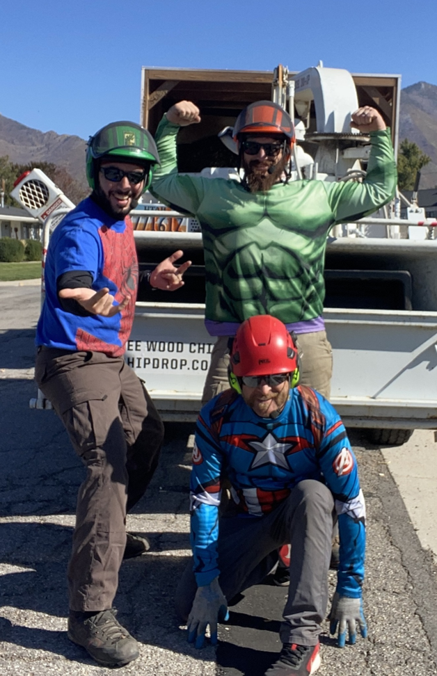 The My Tree Guys, LLC crew in superhero costumes and helmets in front of a tree service truck in Salt Lake City, UT.