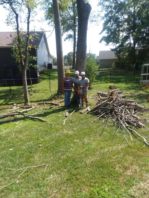A tree service crew with a chainsaw standing next to cut branches and logs after a job by Scotty's Tree Service in Marion, IL.