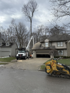 A bucket truck and skid steer from Scotts Tree Experts in Columbus, OH, parked on a residential driveway for a tree service job.