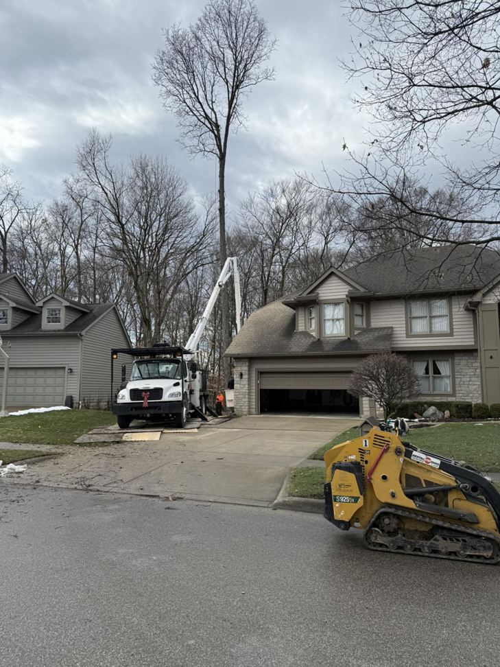 A bucket truck and skid steer from Scotts Tree Experts in Columbus, OH, parked on a residential driveway for a tree service job.
