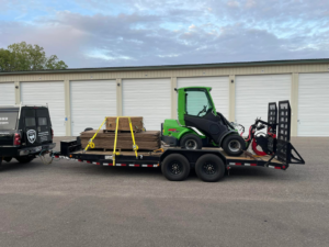 A truck towing a trailer with an Avant mini-loader and wood debris, ready for a tree service job by Canopy Cops Tree Service LLC in Appleton, WI.