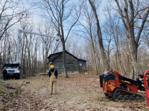 Tree service equipment including a bucket truck and mini skid steer in a wooded area for El tree service in Columbus, OH.
