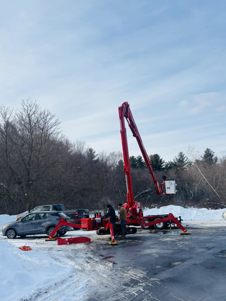 A red spider lift and crew setting up for tree service work in a snowy area by ArbormaxX LLC in Winfield, WV