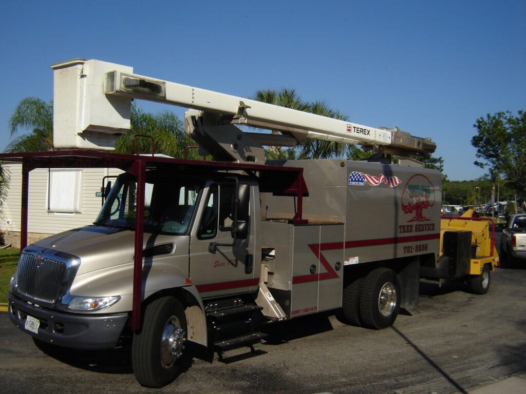 A large tree service truck with a bucket lift and wood chipper trailer for Tim's Tree Service in Cape Coral, FL
