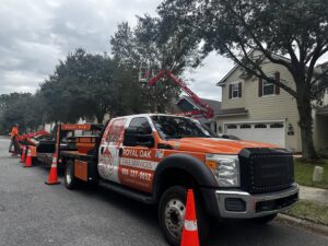 A Royal Oak Tree Services truck with a spider lift on a trailer, parked on a street for a tree service job in Jacksonville, FL.