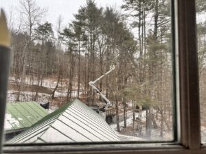 A tree service truck with a boom lift working on trees in a snowy, wooded area, seen from a window, by Teacher's Tree Service in South Burlington, VT.