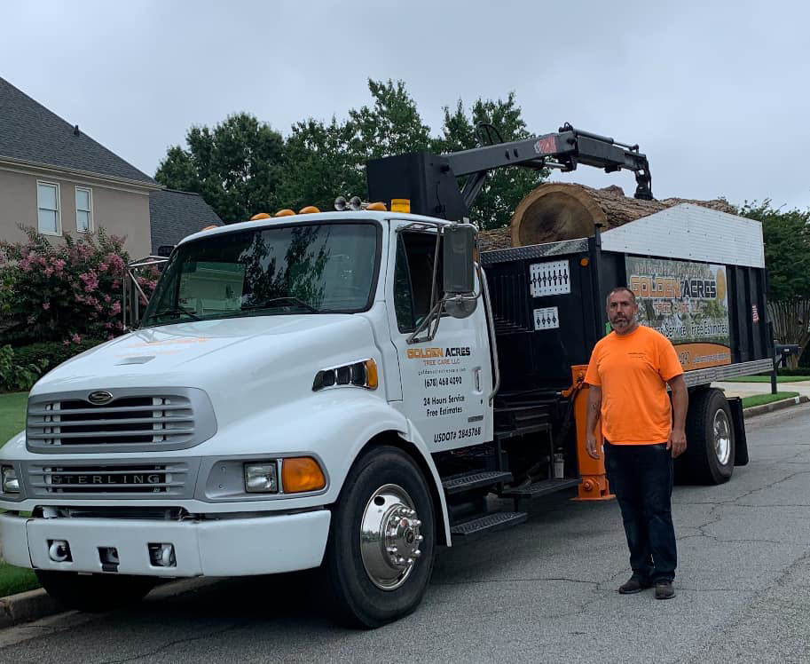 A Golden Acres Tree Care LLC employee stands next to a tree service truck with a large log in the back in Roswell, GA.