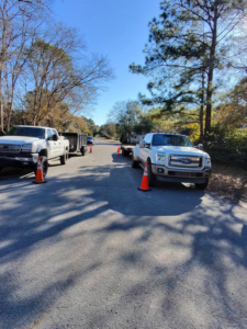 Two tree service trucks with a debris trailer and safety cones set up on a street by TREE Masters Expert Tree Care in Wilmington, NC.