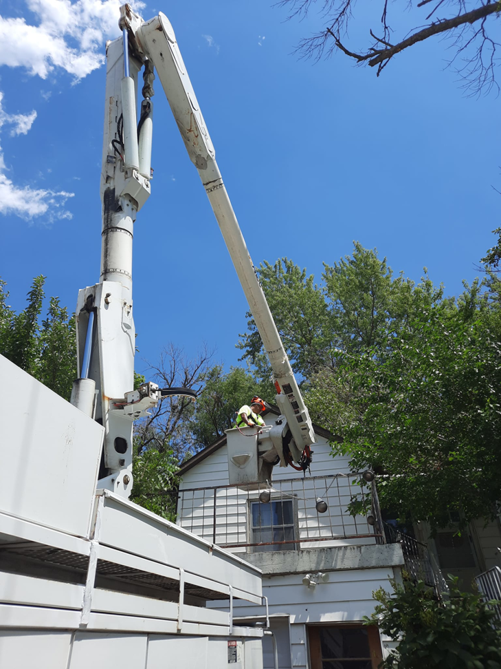 A tree service worker in a bucket truck extended towards a house for trimming by Javier Medina Tree Service LLC in DrDenison, IA.