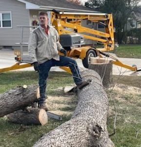 A tree service worker with a chainsaw and an aerial lift after cutting a large tree trunk for S.O.S tree service in Sioux City, IA.