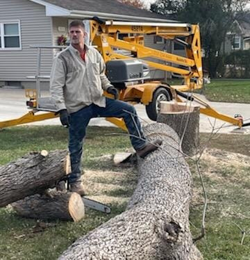 A tree service worker with a chainsaw and an aerial lift after cutting a large tree trunk for S.O.S tree service in Sioux City, IA.