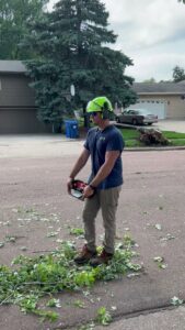 A Patriot Tree Service worker in safety gear holding a chainsaw during branch cleanup in Sioux Falls, SD