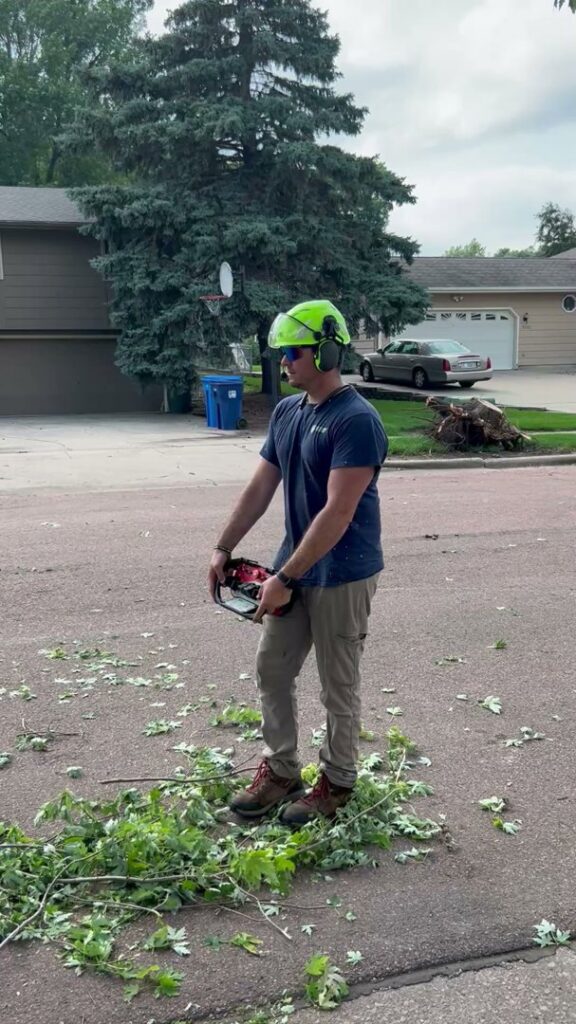 A Patriot Tree Service worker in safety gear holding a chainsaw during branch cleanup in Sioux Falls, SD