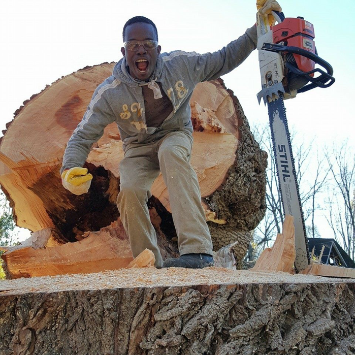 A tree service worker posing with a chainsaw on a large tree stump after removal by WoodChuck Tree Service in Rochester, NY.