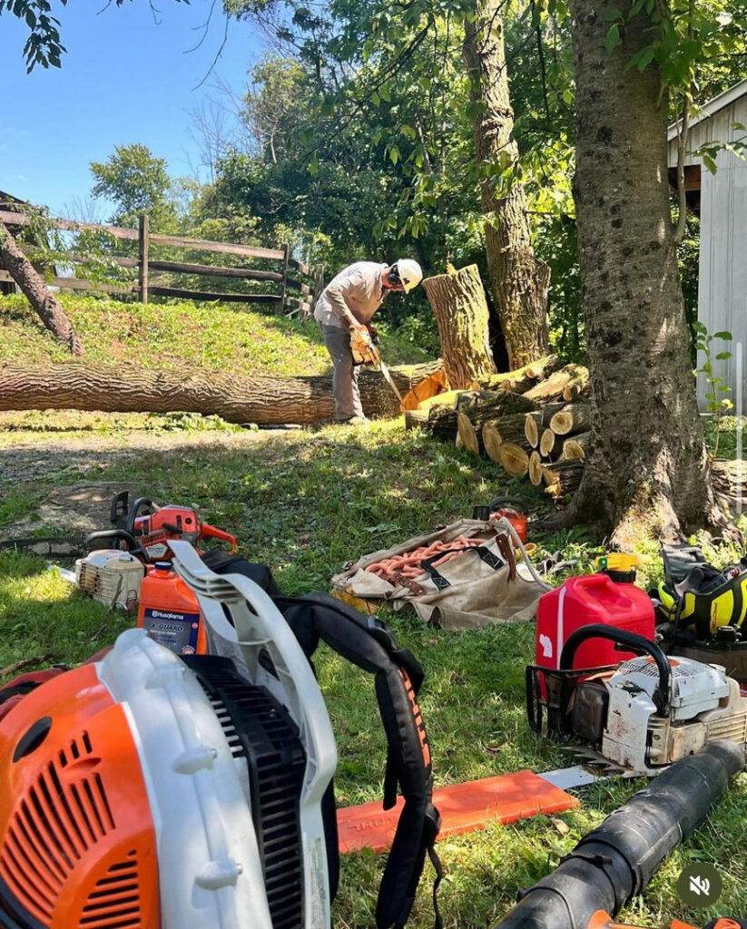 A tree service worker cutting logs with a chainsaw, surrounded by equipment, for PA JB Tree Service in Reading, PA.