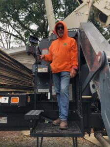 A tree service worker in an orange hoodie standing on heavy equipment, ready for a job with Scott Lanes Tree Service in Chesapeake, VA.