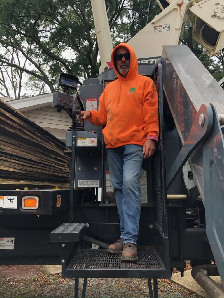 A tree service worker in an orange hoodie standing on heavy equipment, ready for a job with Scott Lanes Tree Service in Chesapeake, VA.