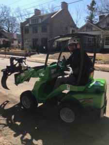 A tree service worker operating a green compact loader with a grapple for Dad's Tree Care Inc. in Kirkwood, Atlanta, GA.