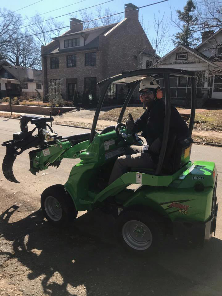 A tree service worker operating a green compact loader with a grapple for Dad's Tree Care Inc. in Kirkwood, Atlanta, GA.