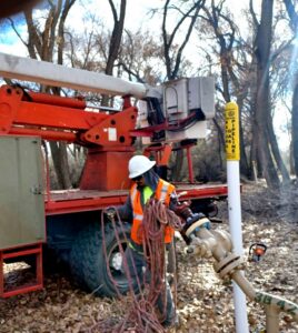 A tree service worker in safety gear holding ropes next to a bucket truck for R and J Tree Service in Farmington, NM.