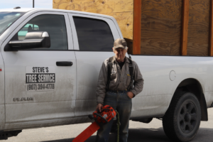 A tree service worker holding a chainsaw next to a Steve's Tree Service truck in Lake Placid, FL.