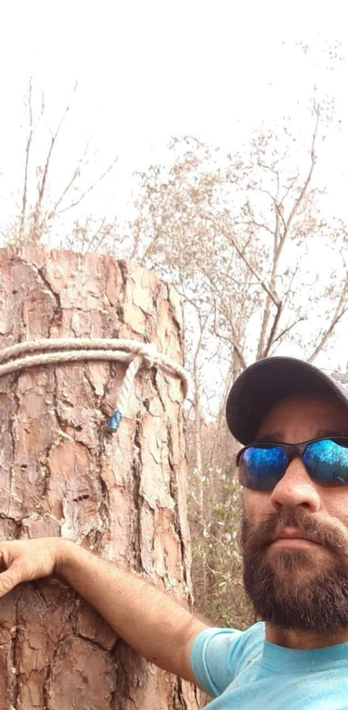 A tree service worker next to a tree trunk with a rigging rope, preparing for work by J.W. Tree Service in Montgomery, AL