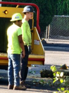 Two tree service workers in safety gear standing near a wood chipper on a job site for D&R Tree Service in Lewiston, ID.