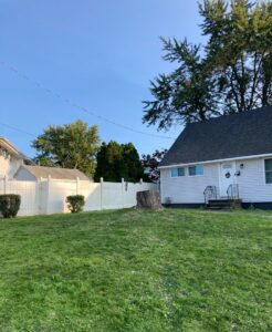 Tree stump in a residential yard next to a house and fence, indicating tree removal by Sky High Tree Service in Lynnwood, WA.