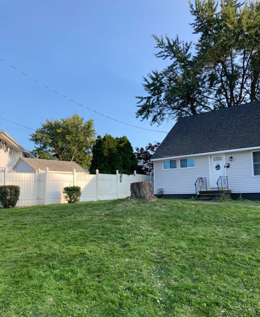 Tree stump in a residential yard next to a house and fence, indicating tree removal by Sky High Tree Service in Lynnwood, WA.