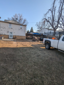A freshly cut tree stump in a backyard with a pickup truck, showing tree removal by S.O.S tree service in Sioux City, IA.