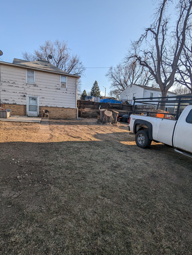 A freshly cut tree stump in a backyard with a pickup truck, showing tree removal by S.O.S tree service in Sioux City, IA.