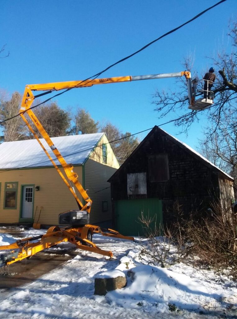 A tree surgeon from Bryan McFadden LLC Tree Surgeon trimming branches with a bucket lift in Auburn, ME during winter.