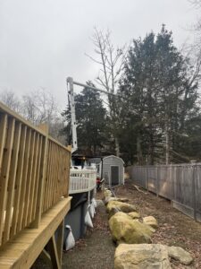A bucket truck from American Tree Service, Inc. performing tree trimming near a residential deck in Coventry, RI.