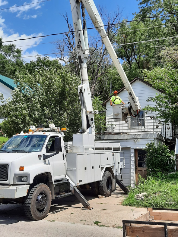 A worker in a bucket truck preparing for tree trimming near a house by Javier Medina Tree Service LLC in DrDenison, IA.