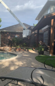 A worker in a bucket trimming a tree near a residential pool for Parker TX Tree Service in Plano, TX.