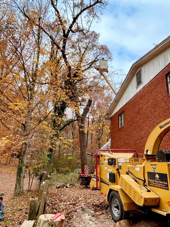 A tree service chipper and bucket truck from Flores Tree Service in Huntly, VA, performing tree trimming near a house.