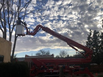 A Kiki's Tree Service arborist in a red boom lift performing tree trimming services in Albuquerque, NM.