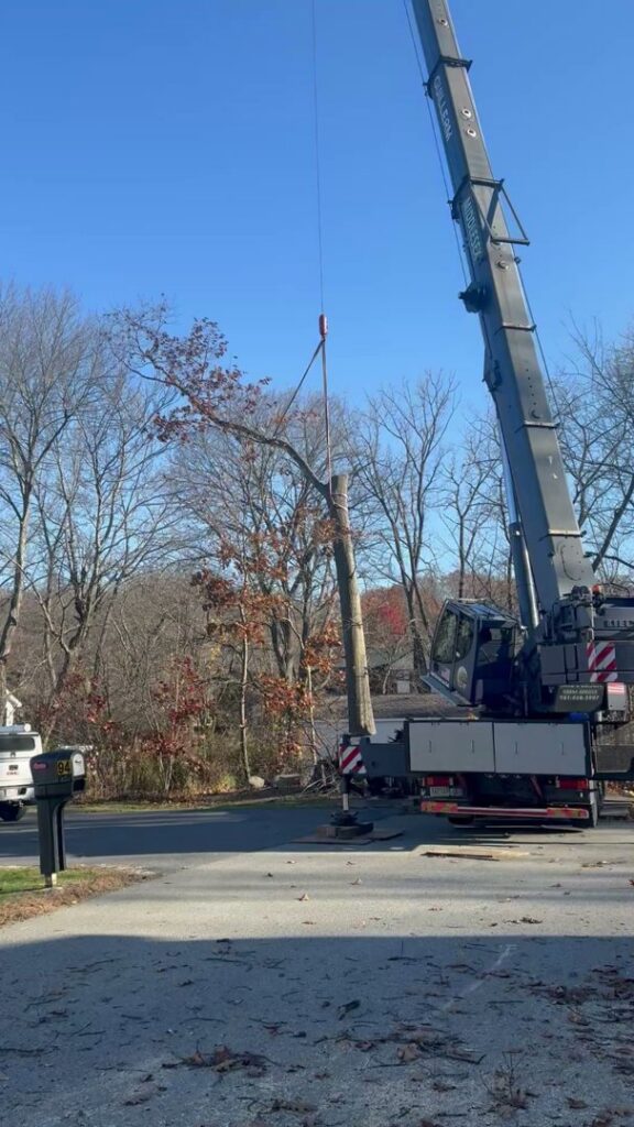 A large crane lifting a section of a tree trunk from a residential area during a tree removal by Tip Top Tree Service in Hudson, NH.