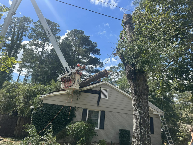 A tree service crew using a bucket lift to remove a large tree trunk section over a house for GNC Tree Service, LLC in Columbia, SC.
