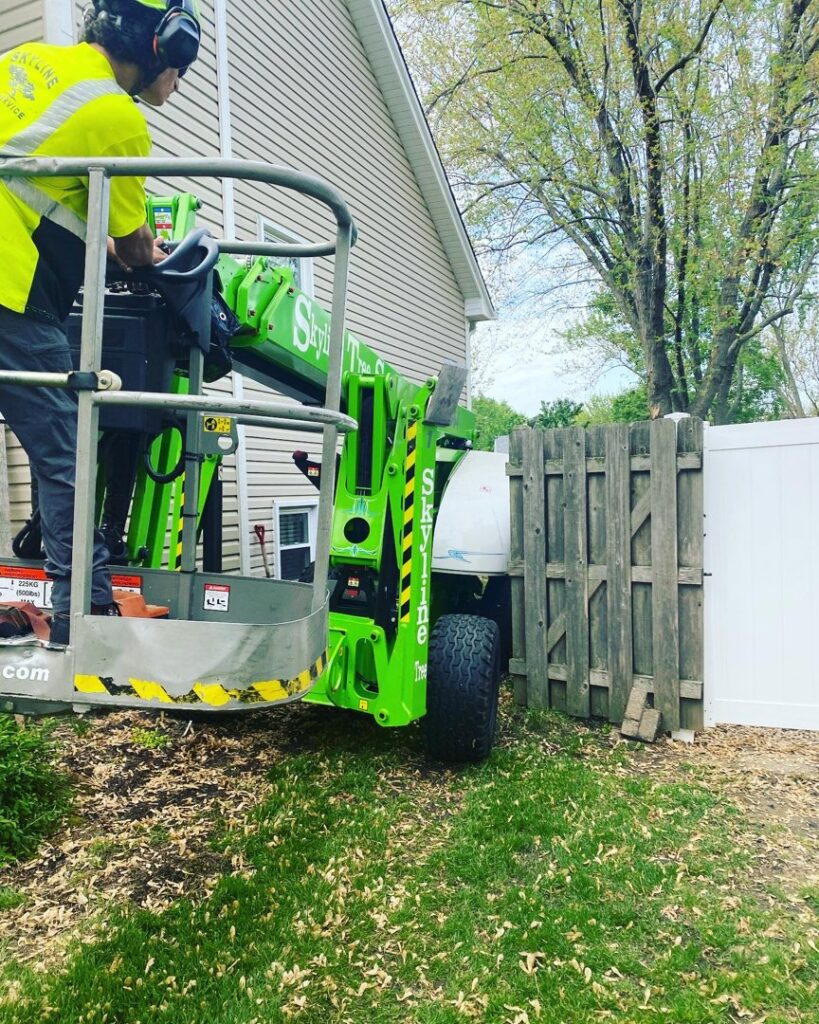 A tree service professional operating a green boom lift during tree work at a residential property by Skyline Tree Service and Landscaping Inc. in Saint Charles, IL.