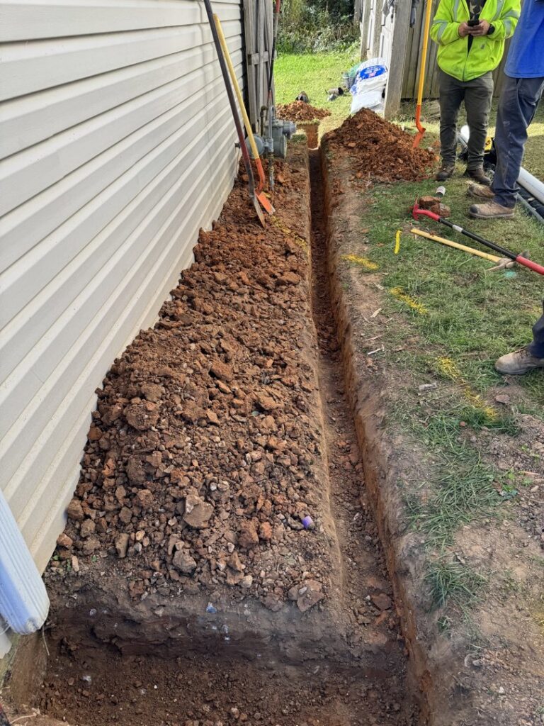 A trench being dug next to a house for irrigation or drainage installation by Rainscapes in Louisville, TN.
