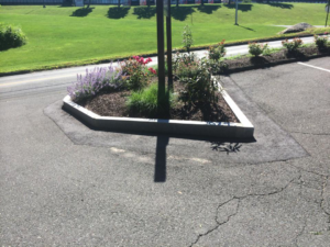 A triangular landscaped island with a stone border and various plants, maintained by Discovery Enterprises LLC in Danbury, CT.