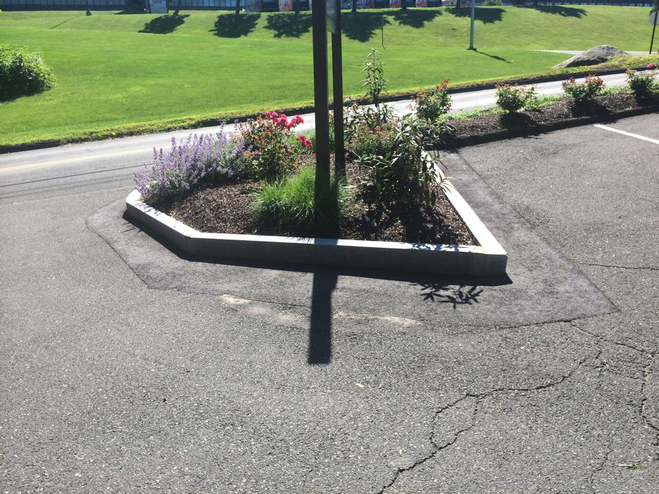 A triangular landscaped island with a stone border and various plants, maintained by Discovery Enterprises LLC in Danbury, CT.