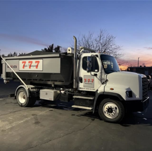 A Triple 7 Dumpsters truck with an empty roll-off dumpster, ready for a junk removal job in Ogden, UT.