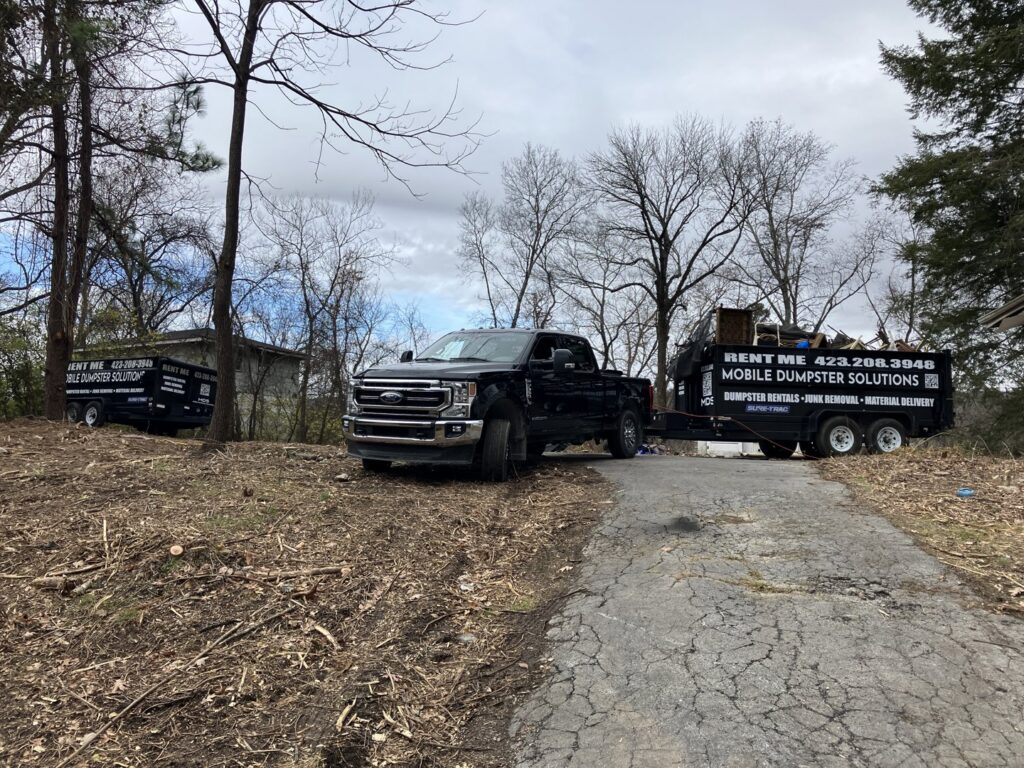 A truck towing a dump trailer from Mobile Dumpster Solutions on a dirt road for junk removal in Chattanooga, TN.