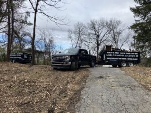 A truck towing a dump trailer from Mobile Dumpster Solutions on a dirt road for junk removal in Chattanooga, TN.