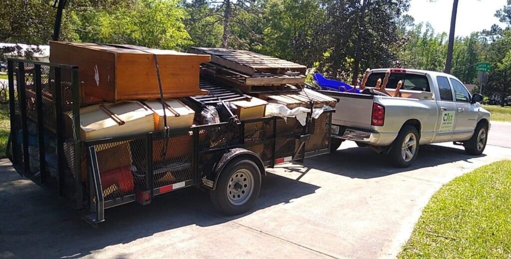A pickup truck pulling a trailer heavily loaded with furniture, pallets, and various junk items, handled by Jax Junk Squad in Jacksonville, FL.