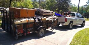 A pickup truck pulling a trailer heavily loaded with furniture, pallets, and various junk items, handled by Jax Junk Squad in Jacksonville, FL.