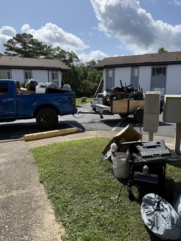 A blue pickup truck and trailer loaded with various items, with more junk piled nearby, for removal by Reliable Pro in Tallahassee, FL.