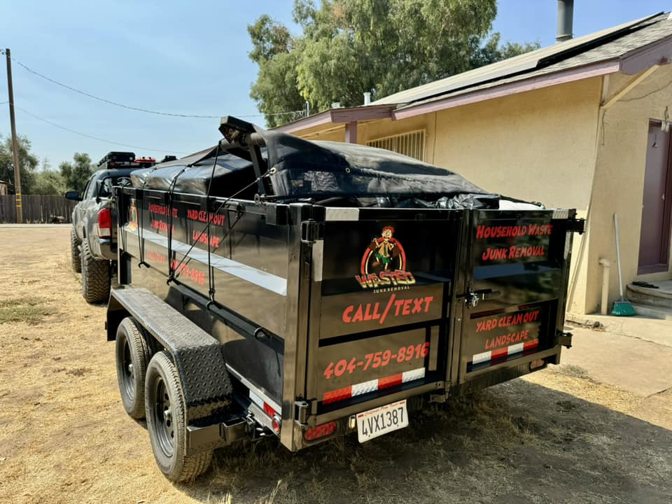 A Wasted Junk Removal truck and trailer loaded with junk and covered by a tarp, ready for disposal in Corona, CA.